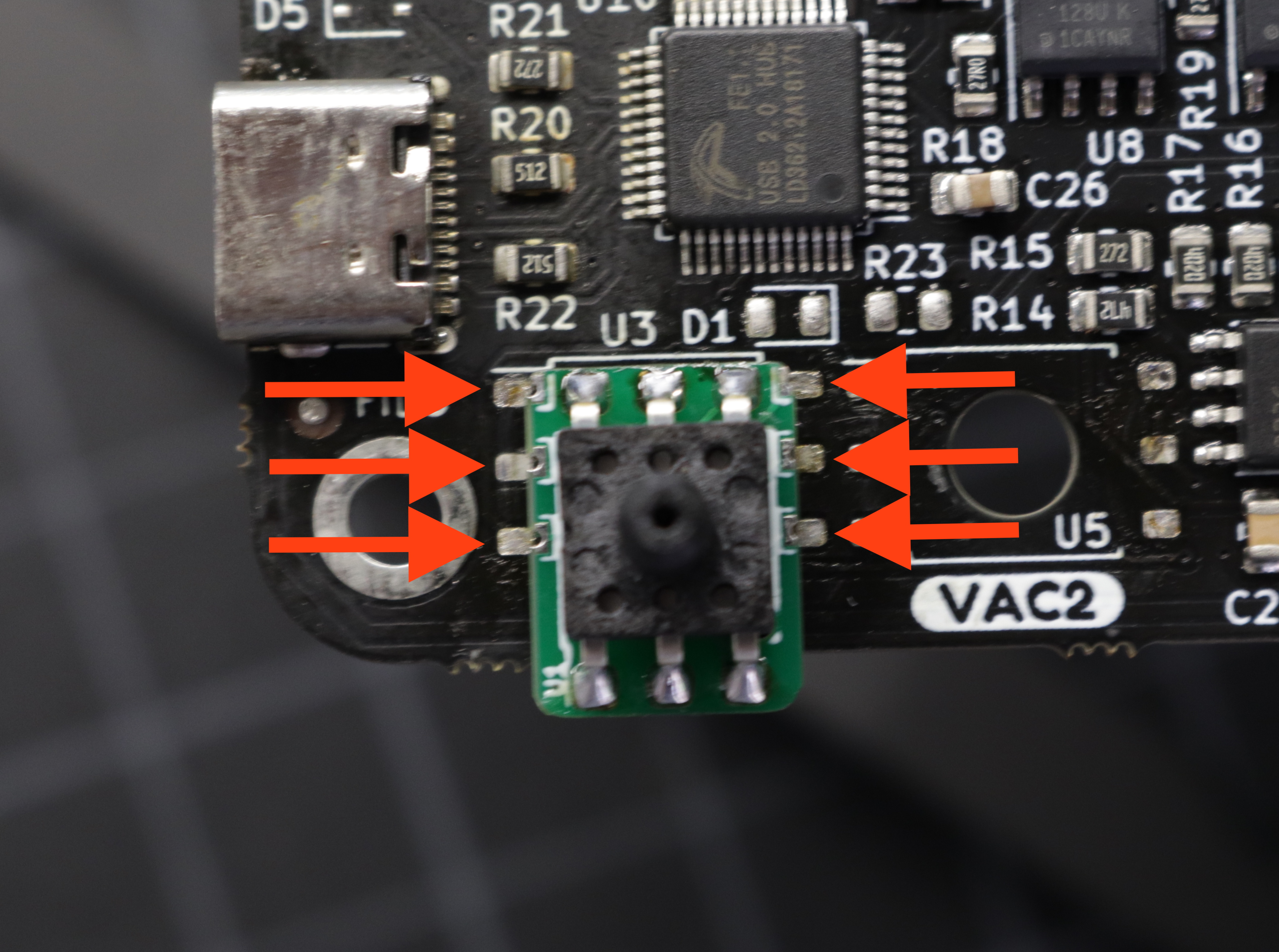 A photo of the interposer on the motherboard from above, with red arrows pointing to the six plated edges of the interposer matching with the 6 pads on the motherboard